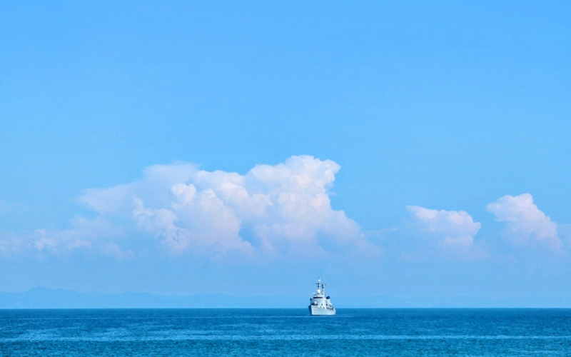 青空の下、穏やかな海を一隻の船が進む風景