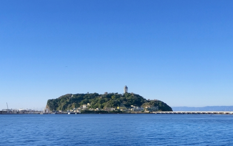 青空の下、海の向こうに江の島が見える湘南の風景。TUBEの夏を思わせる景色。