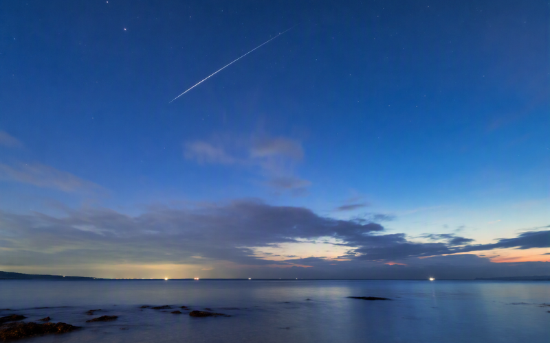 夜明け前の海に広がる星空と、静かに流れる一筋の流れ星