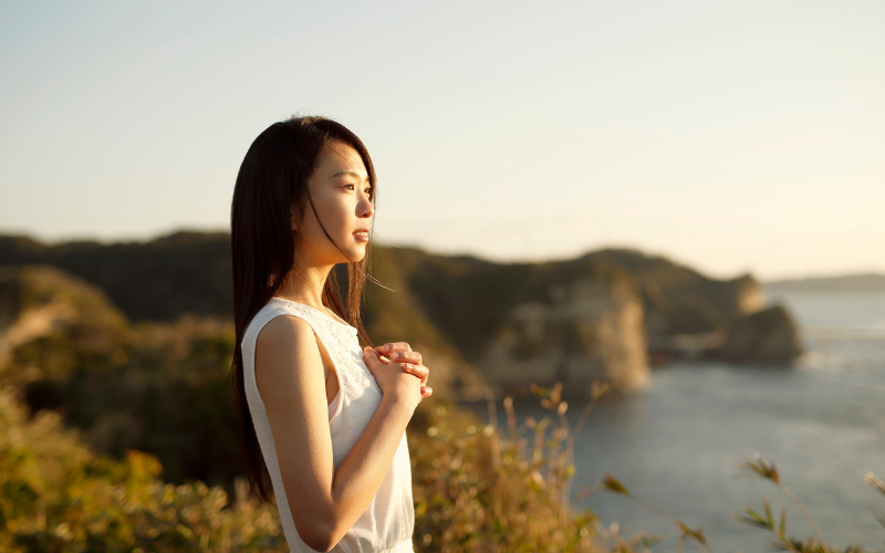 海を見つめながら祈るように立つ女性の横顔